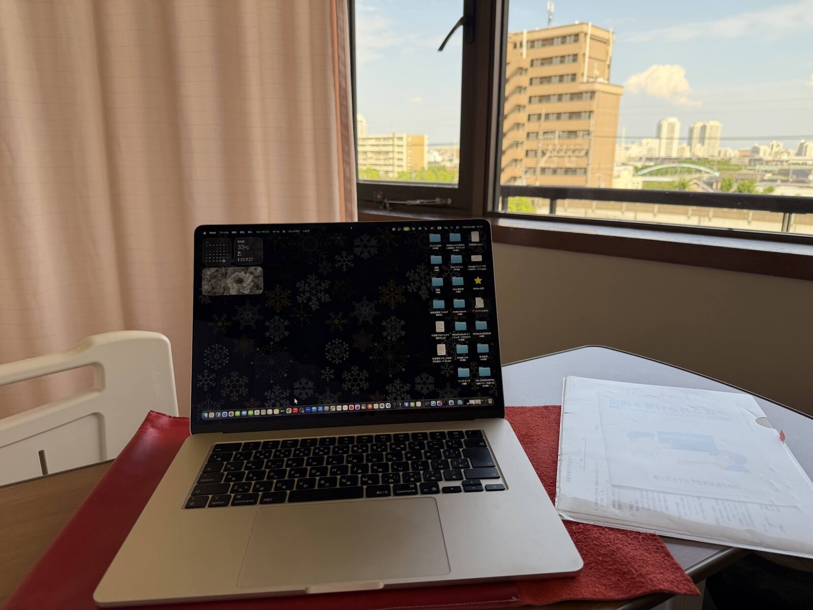 病室のテーブルの上で開いたMacBookと、窓の外の街並み