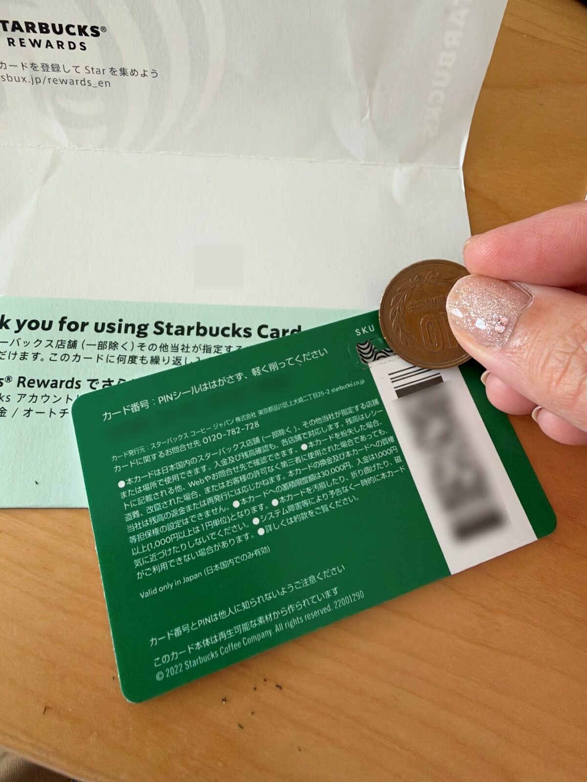 10円玉でカード裏面の銀色の部分を軽くこすっている手元の写真（カード番号にはぼかしをかけています）